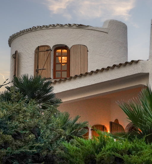 Vista exterior de una villa mediterránea blanca con torre redonda y jardín.
