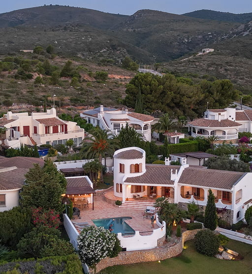 Vista panorámica de un complejo de villas mediterráneas con piscina y montañas.