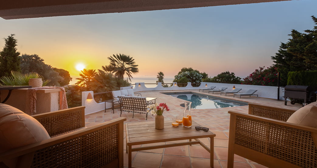 Sillones de exterior en una terraza con piscina y vistas al atardecer sobre el mar.