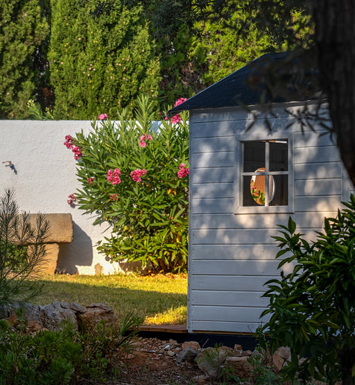 Casita blanca de madera en un jardín con flores al atardecer.