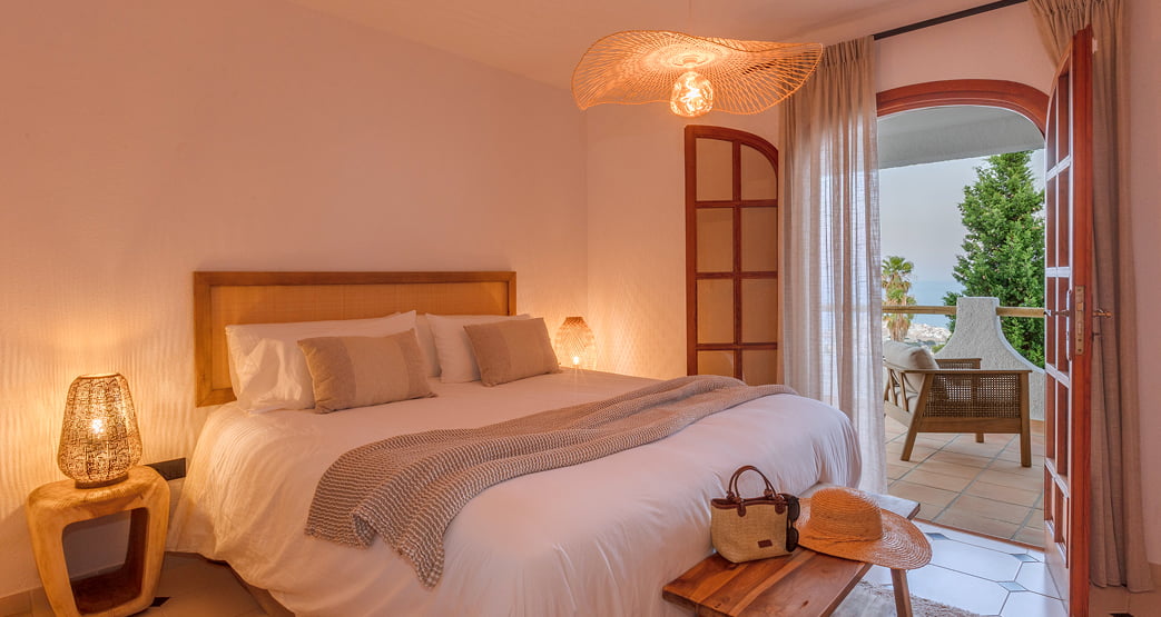 Cama doble en una habitación luminosa con balcón y vistas al exterior.